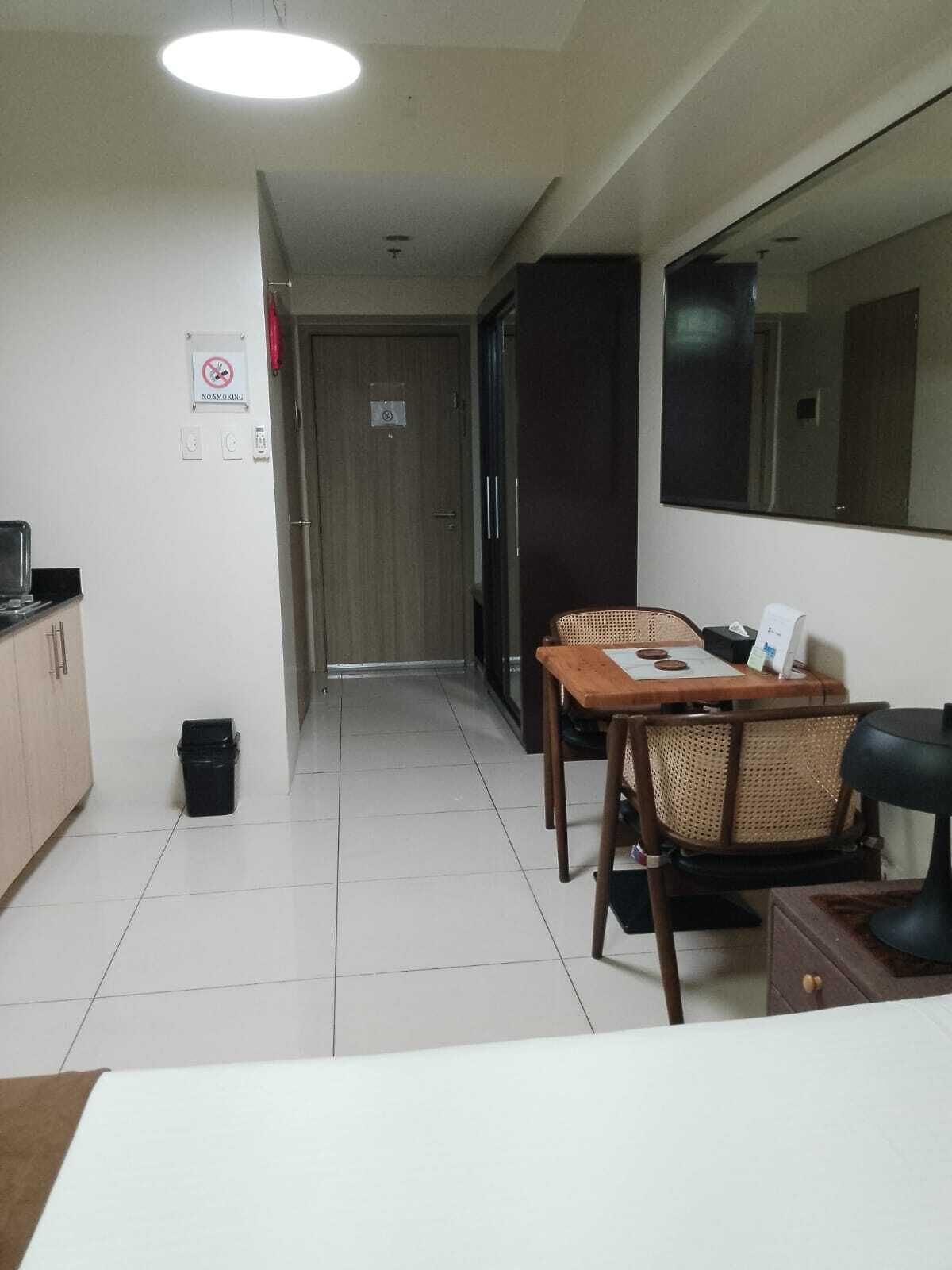 Et lille hotelværelse med tekøkken, spiseplads med bord og stole, et stort spejl og en dør til et andet værelse.