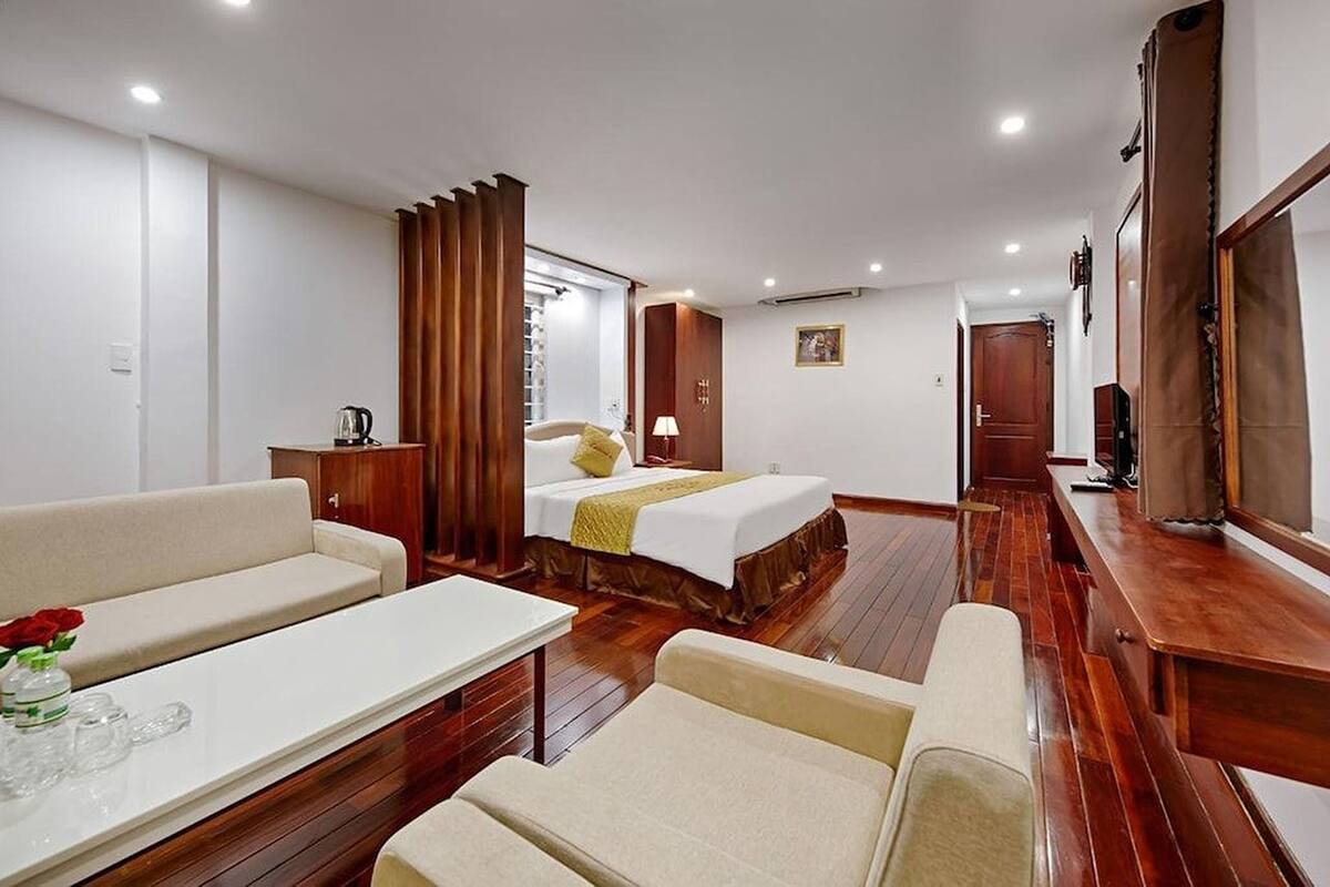 Quarto de hotel com cama, sofá, mesa com um vaso de flores e um banco de madeira.