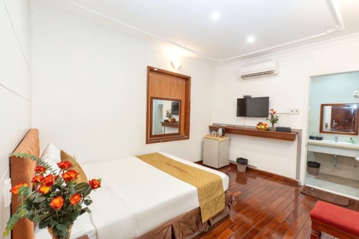 A hotel room with a bed, a desk, a TV, a mirror, and a bathroom.