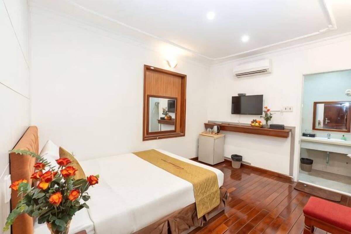 Quarto de hotel com cama, escrivaninha, televisão, espelho e banheiro.