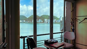 A room with a view of a body of water, a chair, a table with a tray, and a coat rack. - Le Pont Bungalow Hostel (Hai Phong)