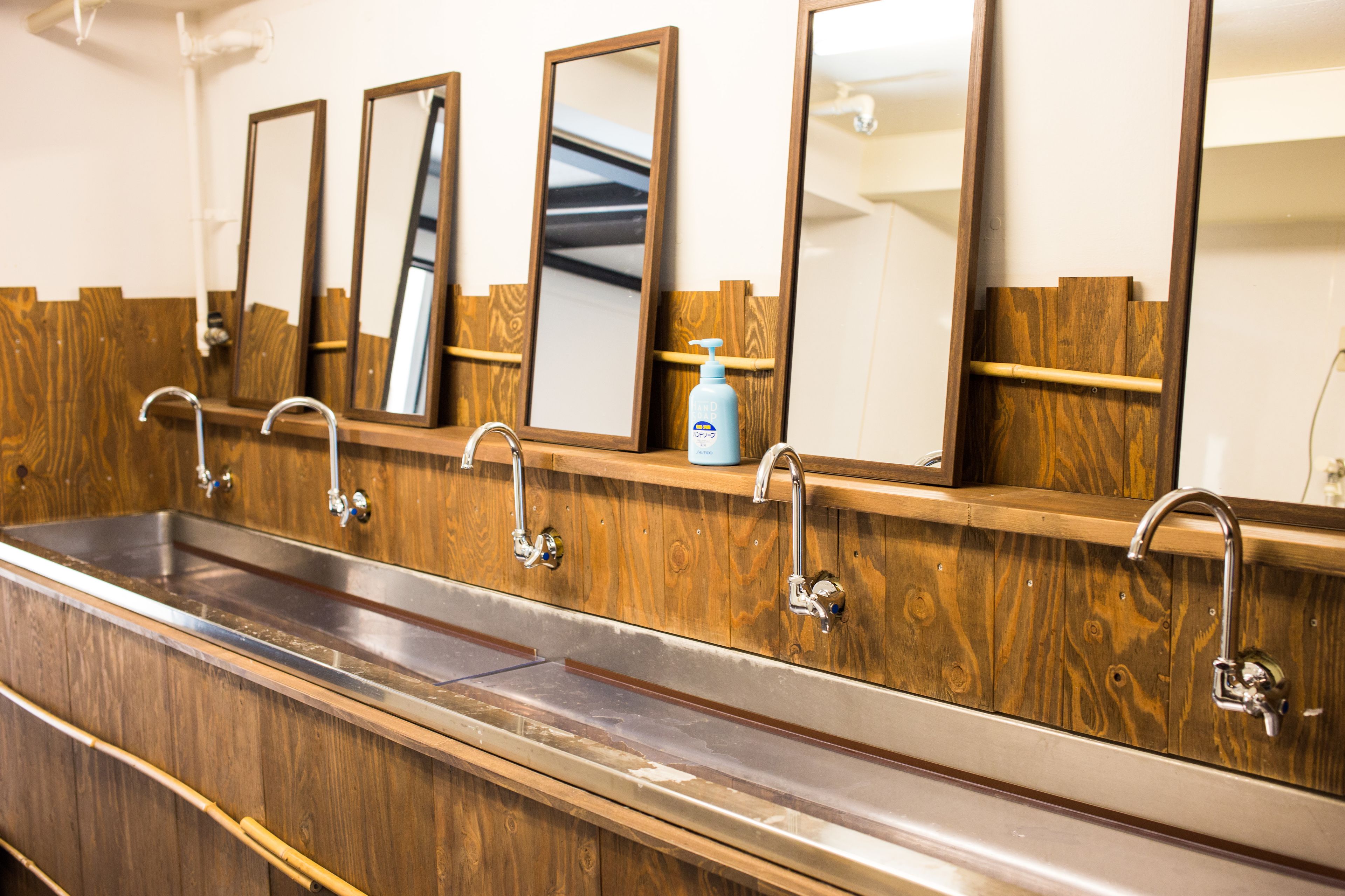 Eine öffentliche Toilette mit Holztresen, mehreren Spiegeln und Edelstahlwaschbecken.