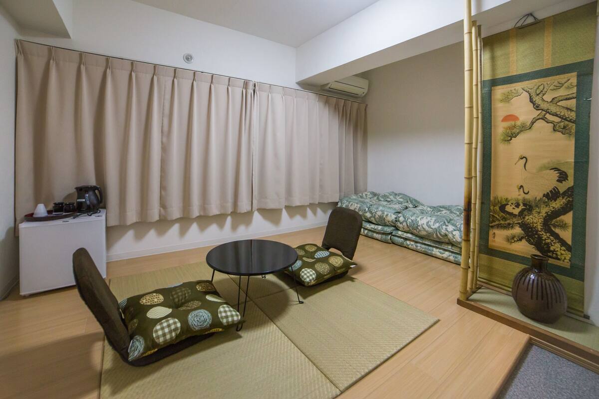 A room with a bed, a small table with chairs, a coffee maker, and a painting on the wall.