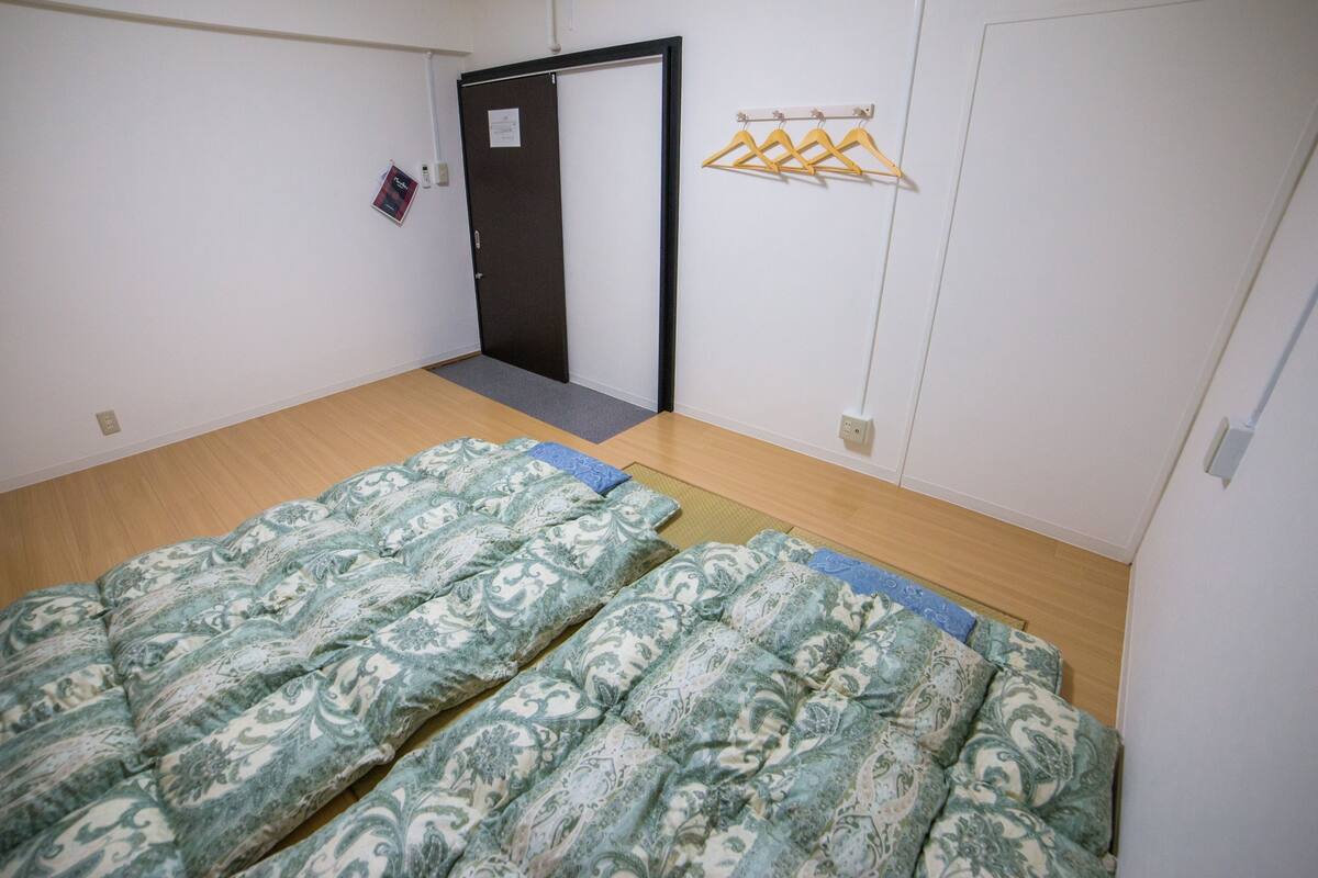 A room with two beds, a door, a coat rack, and a small mat.