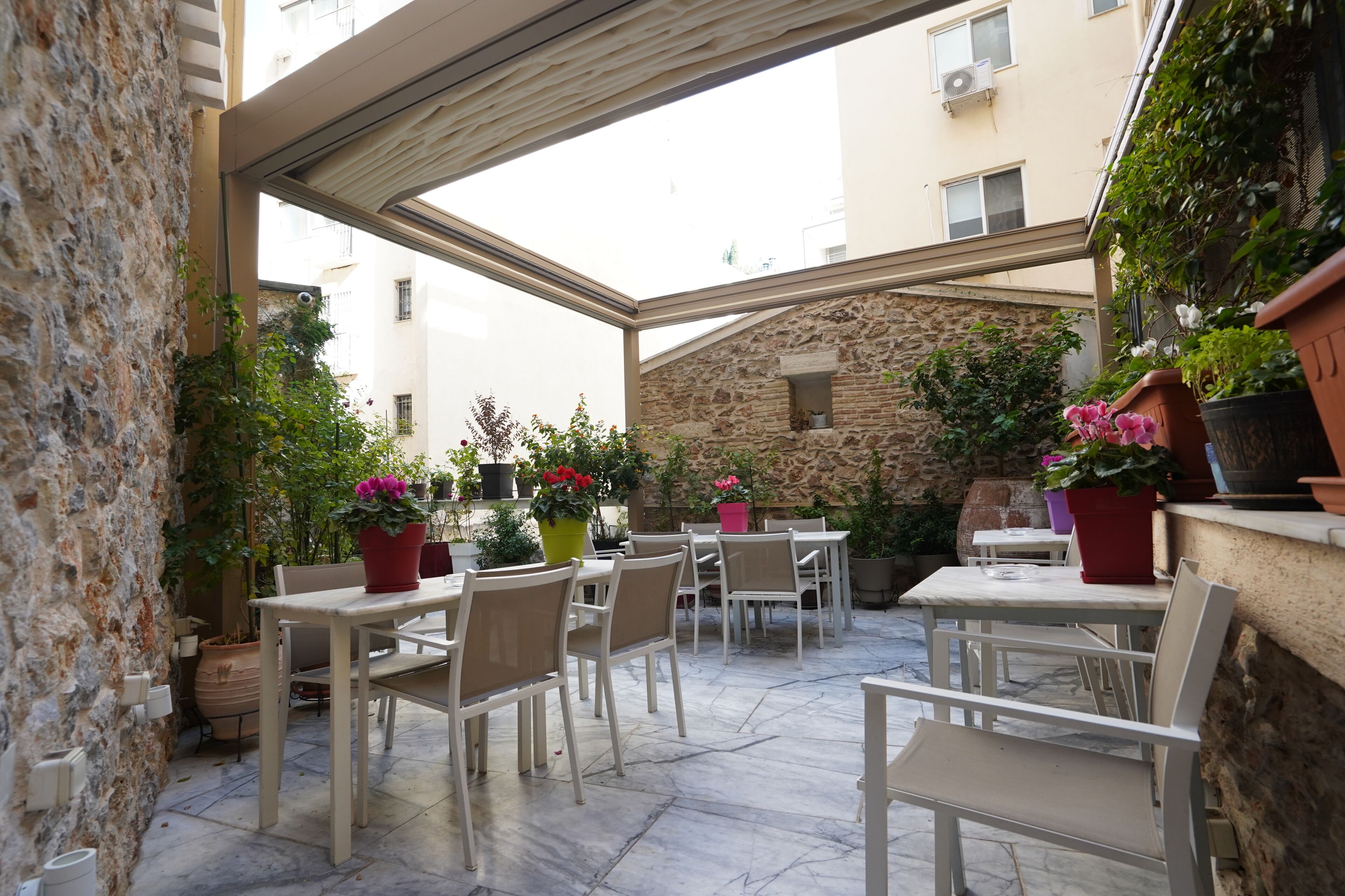 An outdoor patio with tables and chairs, surrounded by stone walls and potted plants.
