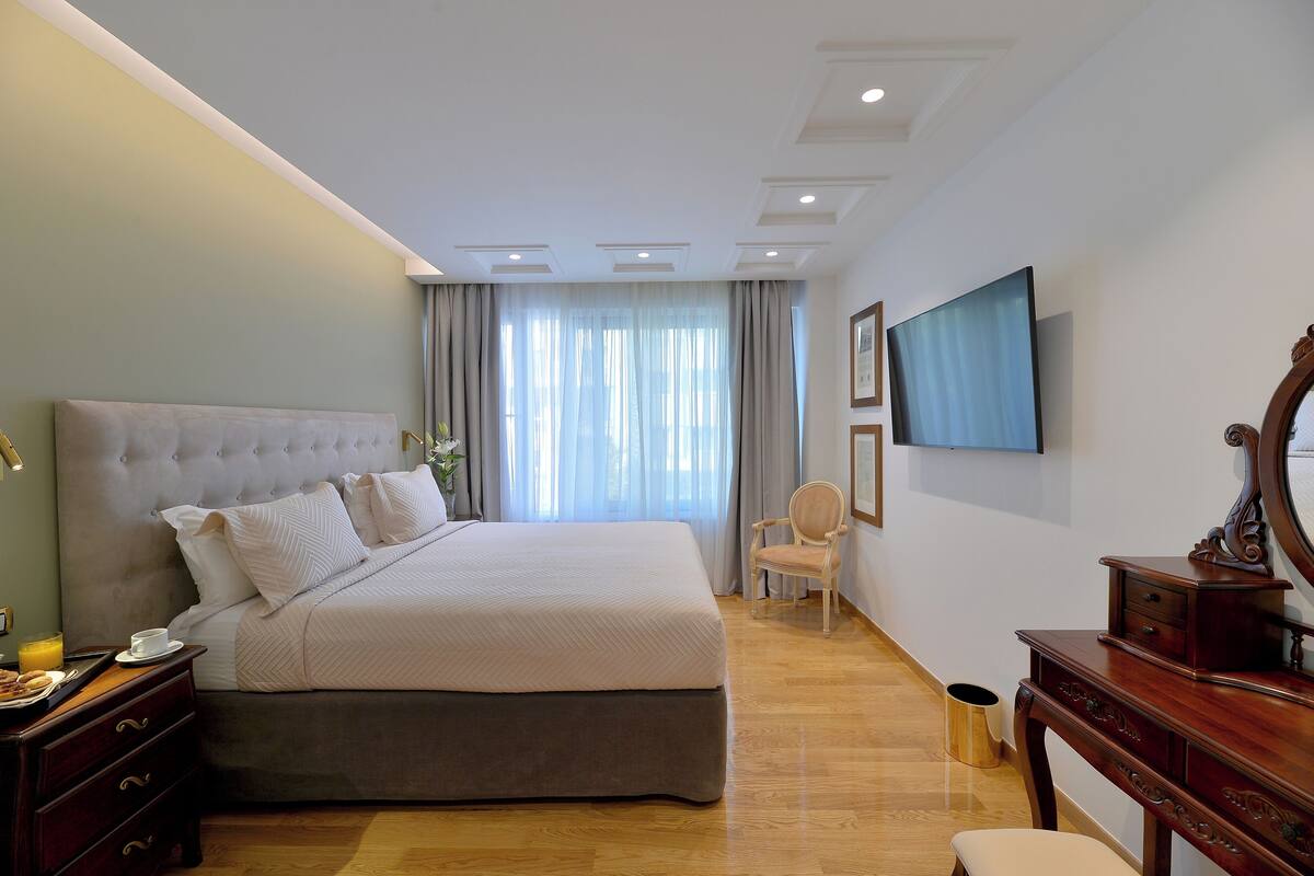 A modern bedroom with a large bed, a wooden dresser, a chair, and a flat-screen TV mounted on the wall.