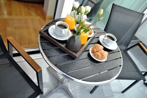 A round dining table with a tray holding croissants, two cups of coffee, a vase with flowers, and a glass of orange juice. - Acropolian Spirit Boutique Hotel (Athens)