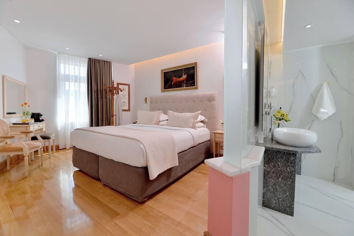 A modern hotel room with a large bed, a bedside table, a desk, and a bathroom with a marble sink.