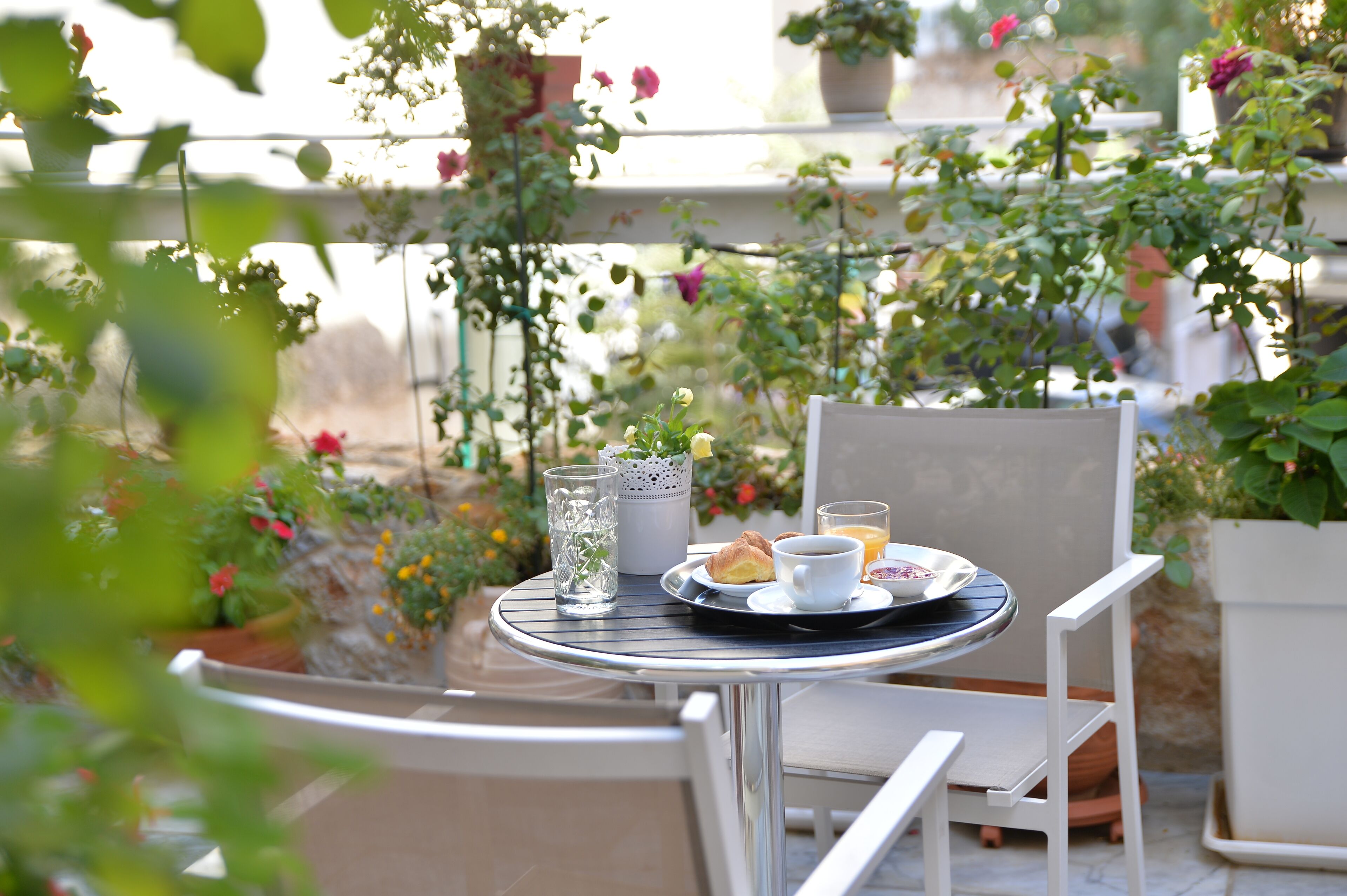 A round table with a white chair, a glass of water, a cup of coffee, a croissant, and a plate with a croissant and a slice of orange.