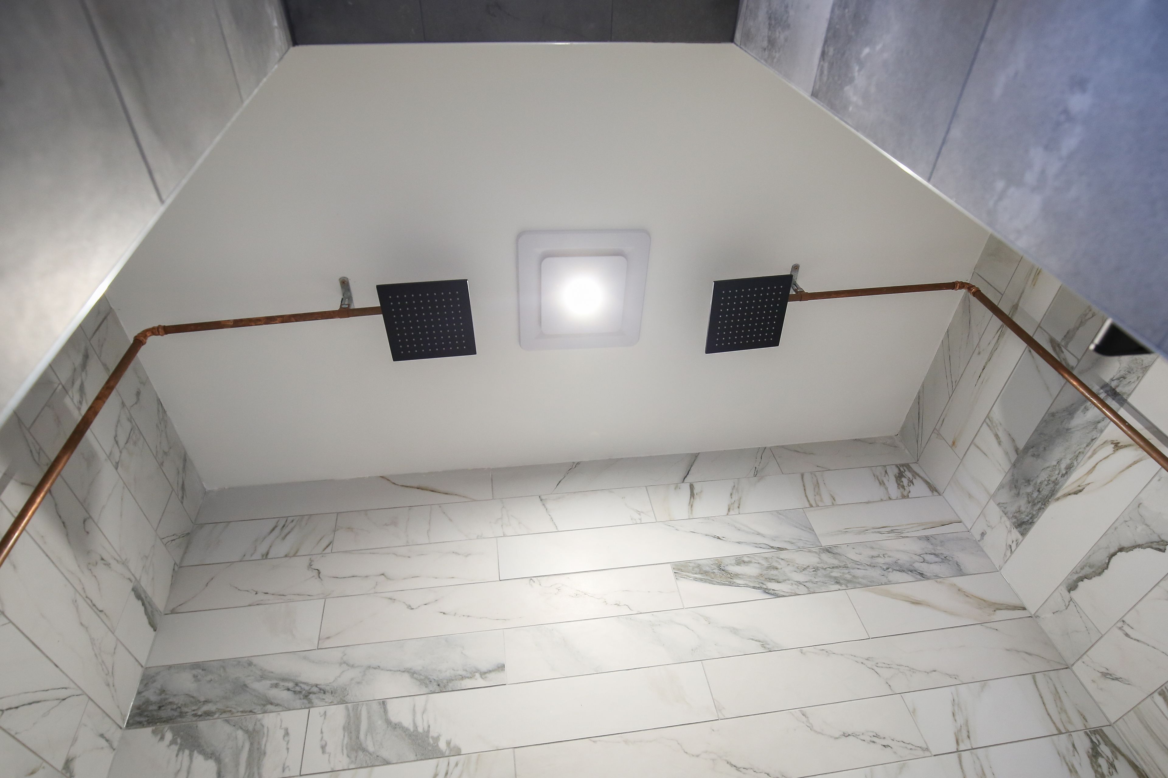 Een badkamer met een wit plafond, een marmeren vloer en een zichtbare douchehoek.