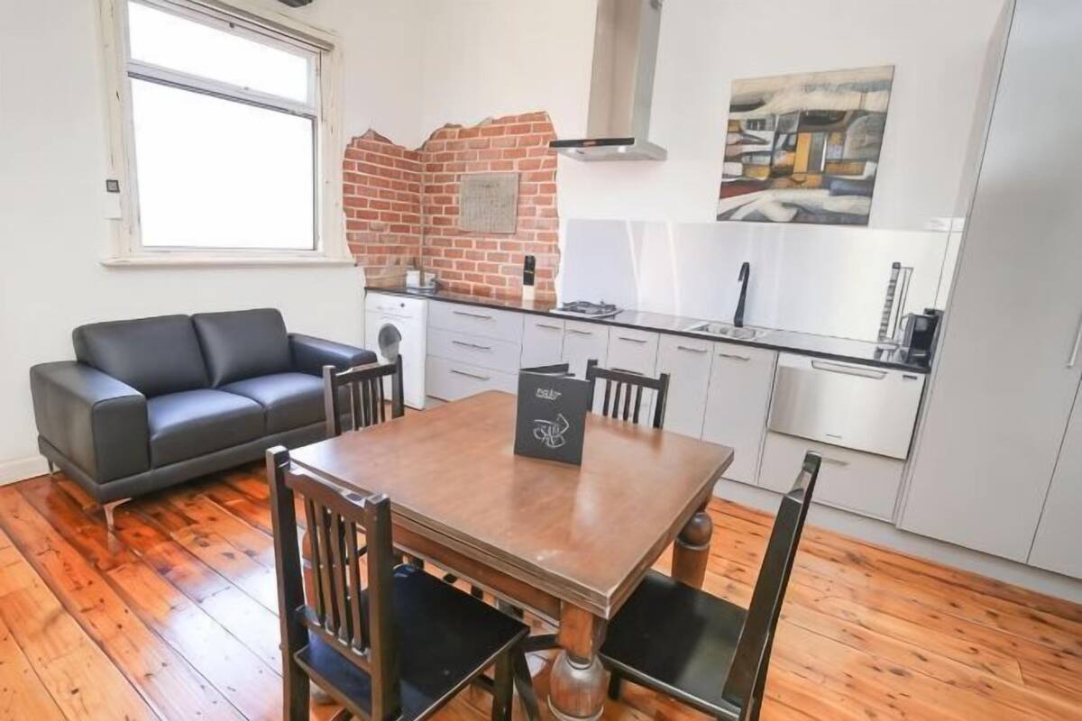 A compact kitchen with a brick backsplash, modern appliances, and a dining area with a wooden table and chairs.