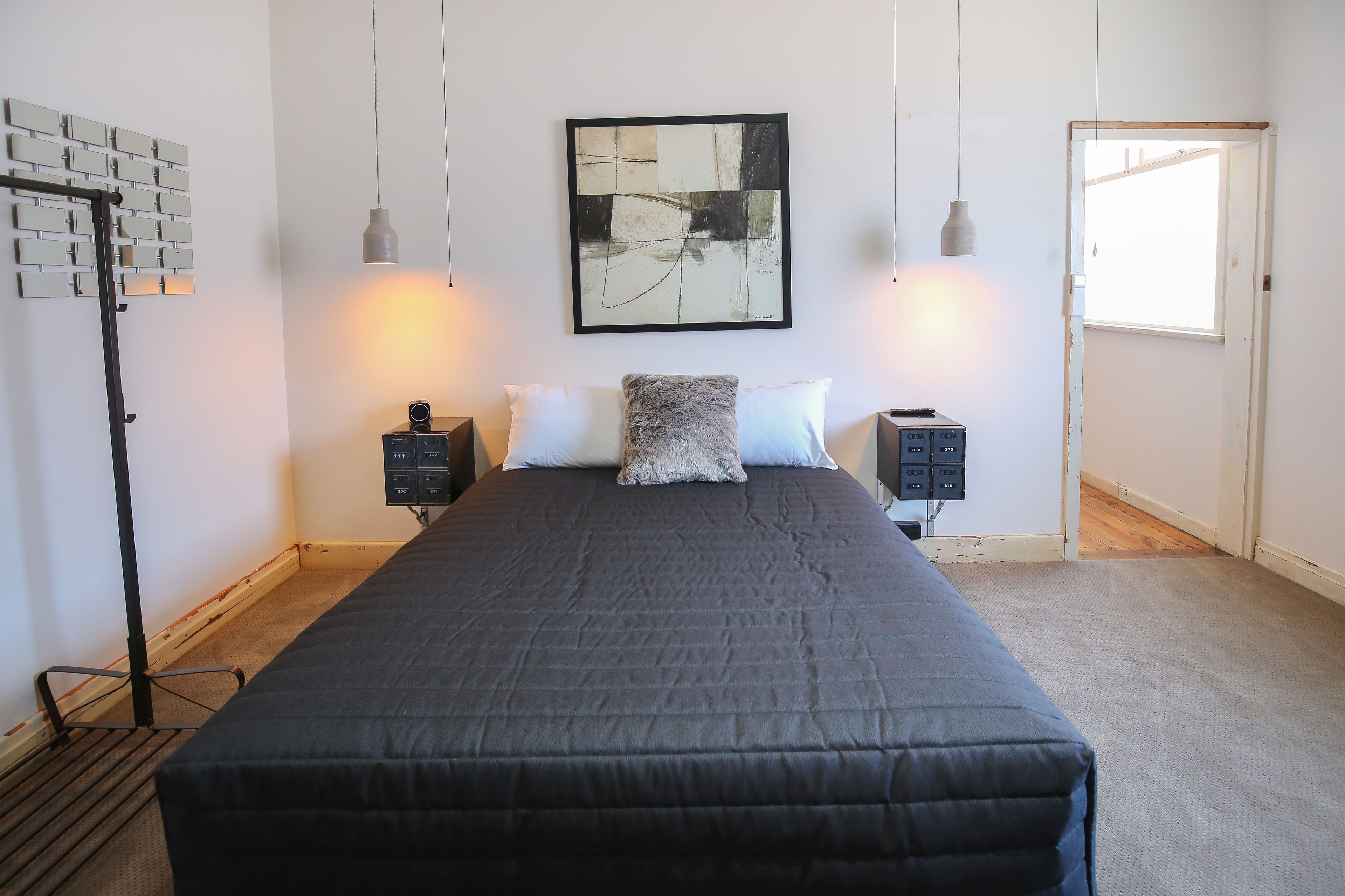 Een slaapkamer met een groot bed, twee nachtkastjes, een abstract schilderij aan de muur, en een raam.