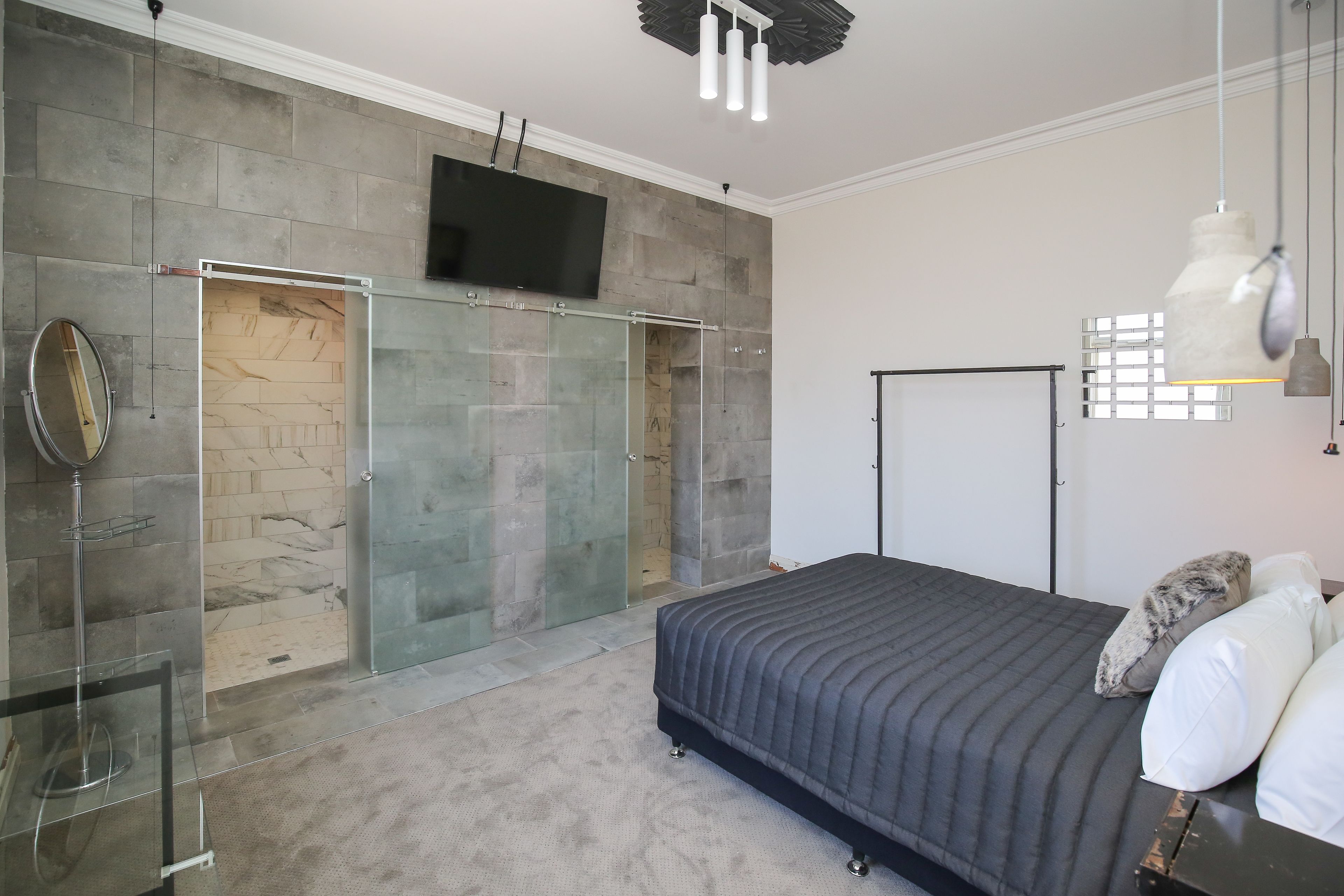 Ein modernes Schlafzimmer mit einem großen Bett, einem an der Wand montierten Fernseher und einer Duschkabine aus Glas.