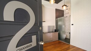 A modern bathroom with a glass shower enclosure, a marble-tiled wall, and a wooden floor. - Indulge Apartments -The Urban Collection (Mildura)