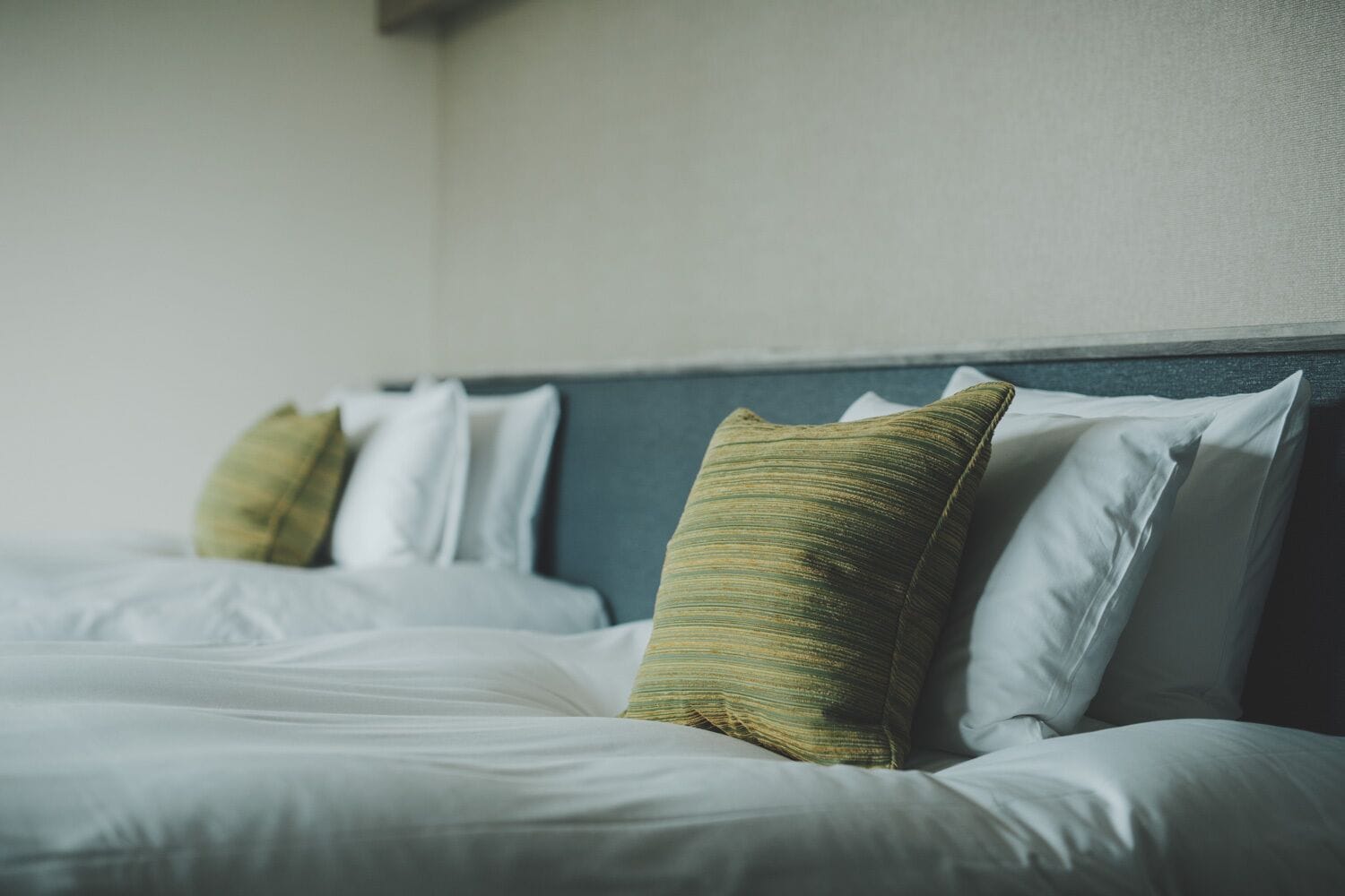 Een opgemaakt bed met witte lakens en groene en witte kussens.