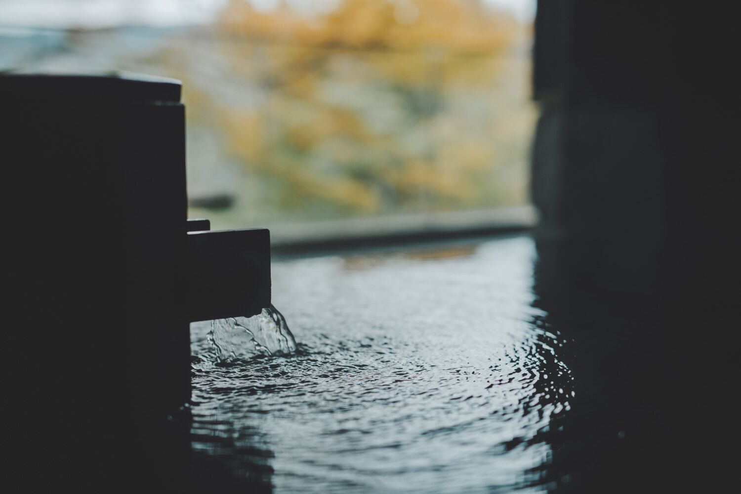 Wasser fließt aus einem Wasserhahn auf eine spiegelnde Oberfläche.
