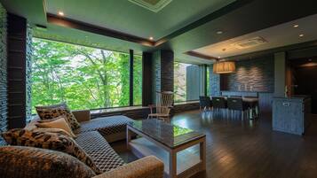 A modern living room with a large window, a sofa, a dining area, and a kitchen.