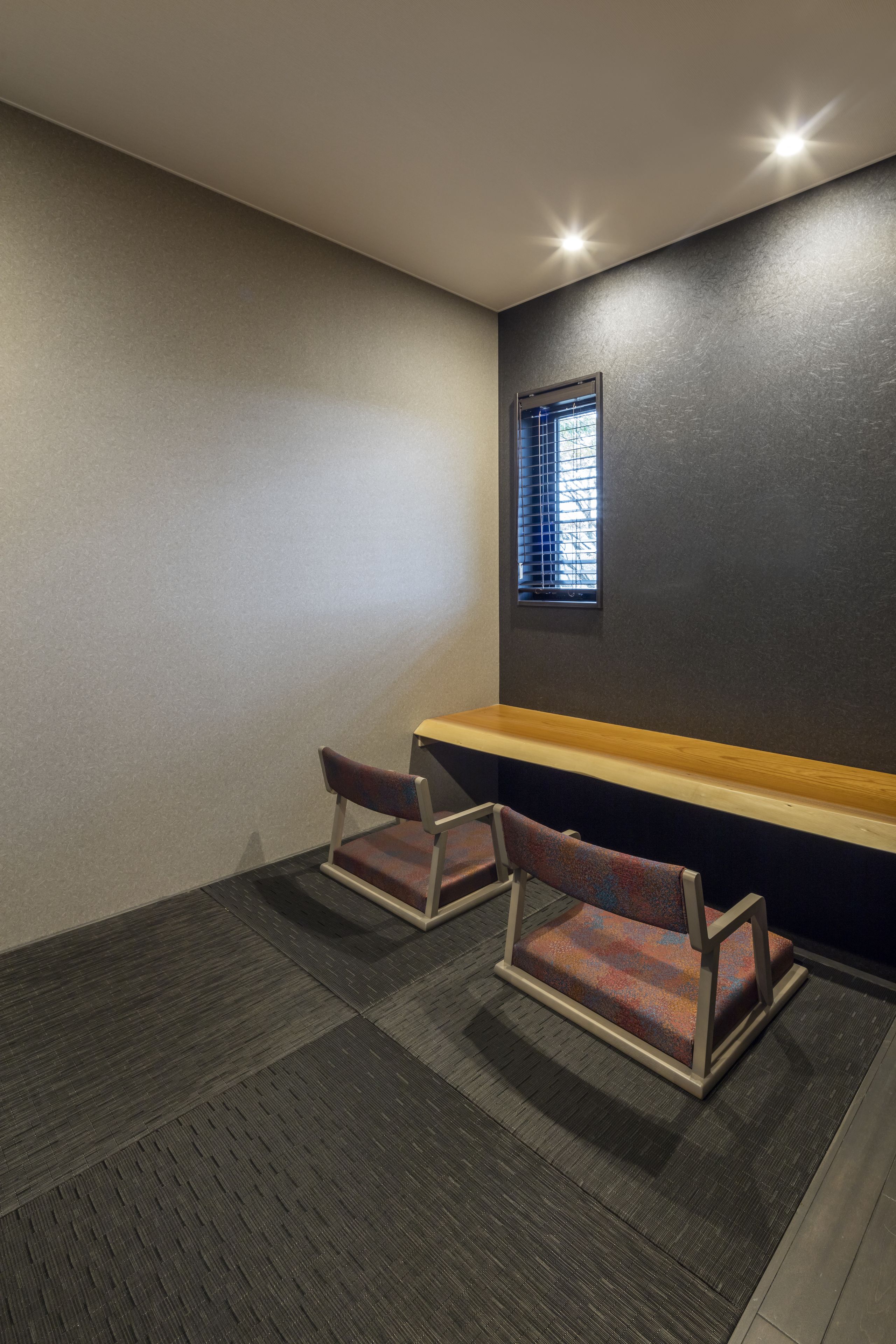 A room with two chairs, a bench, a small window, and a dark wall.