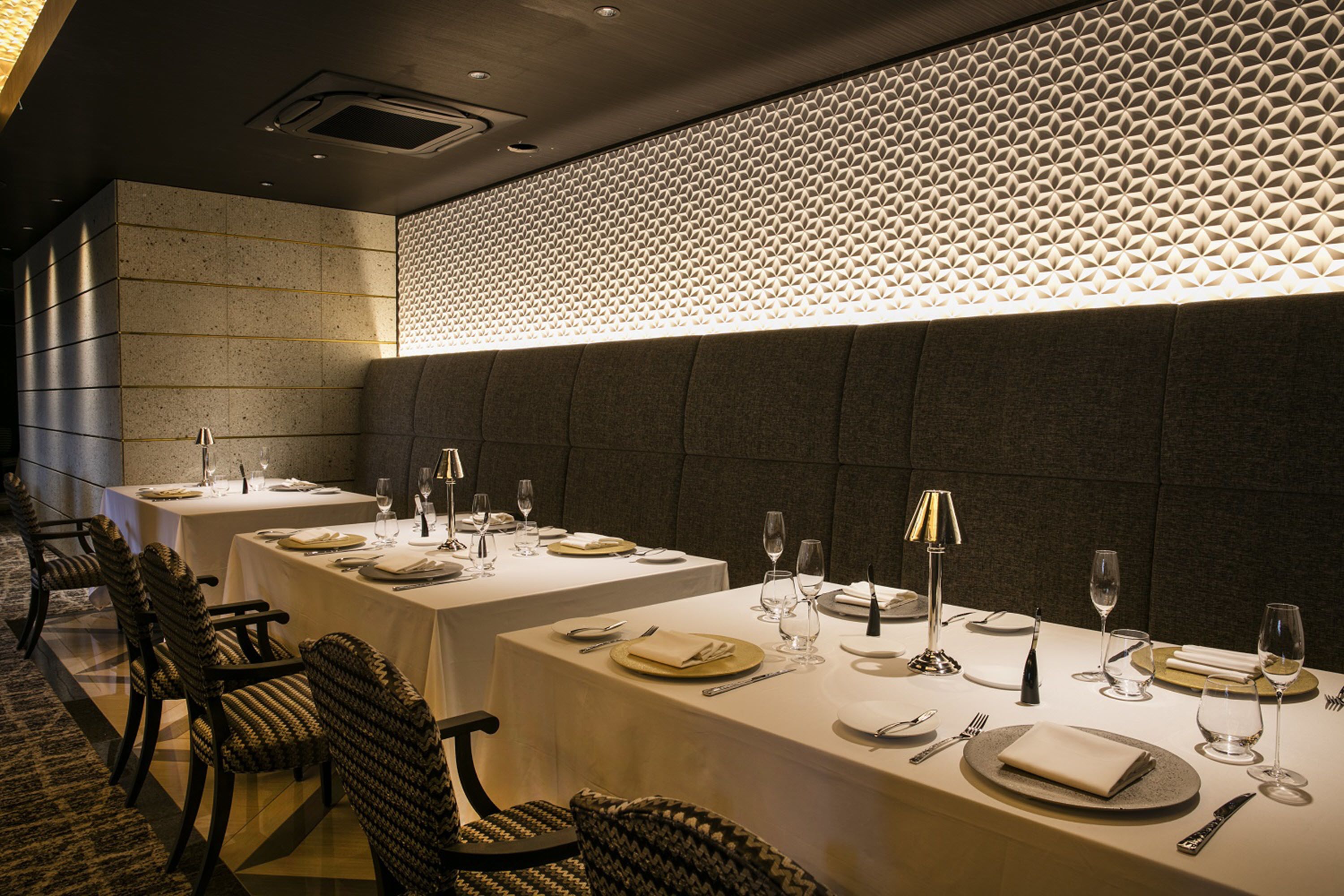Un comedor con mesas dispuestas para dos, con un diseño de pared estampado y un diseño de techo moderno.