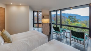 A modern hotel room with two beds, a small kitchenette, and a balcony with a view of mountains.