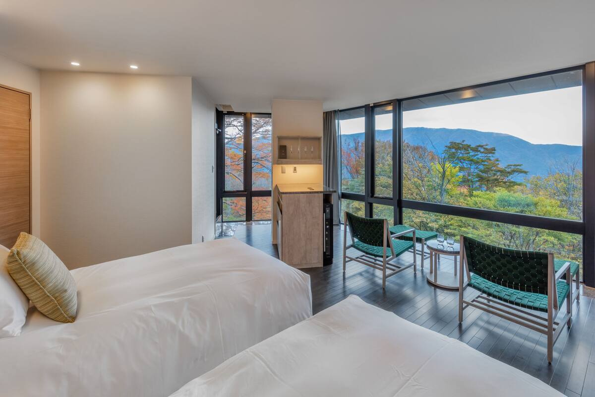 Ein modernes Hotelzimmer mit zwei Betten, einer kleinen Küchenzeile und einem Balkon mit Bergblick.