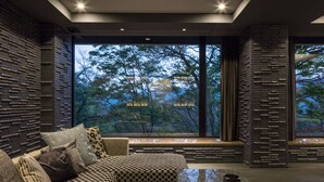 A modern living room with a patterned sofa, a coffee table, and a large window offering a view of trees.