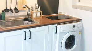 Eine kleine Küche mit einer eingebauten Waschmaschine, einem Spülbecken und hängenden Küchenutensilien.