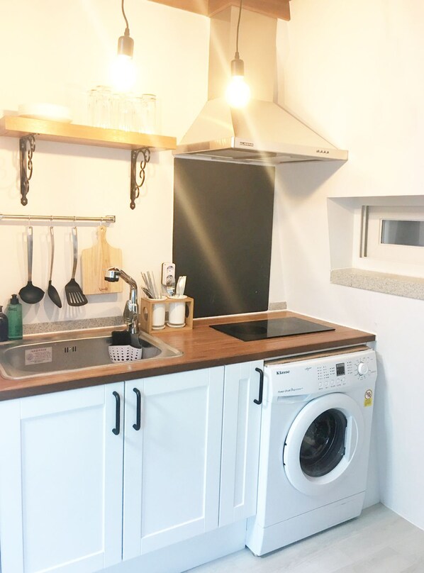 A compact kitchen with a built-in washing machine, a sink, and hanging utensils.