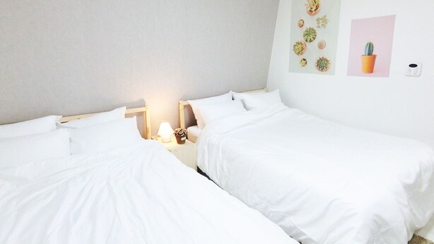 Ein Hotelzimmer mit zwei Einzelbetten, einem Nachttisch mit Lampe sowie Wandbildern, darunter eine Kaktusdarstellung.