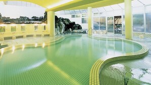 Une piscine intérieure au design incurvé, avec un sol carrelé et une formation rocheuse en arrière-plan.
