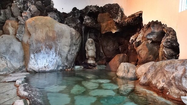 Une étendue d’eau claire, parsemée de rochers et ornée d’une statue, le tout situé dans un espace rocheux.