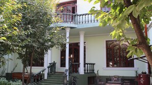 A courtyard with a staircase leading to a balcony, surrounded by greenery and a seating area with a table and chairs. - Green House Hostel (Dushanbe)