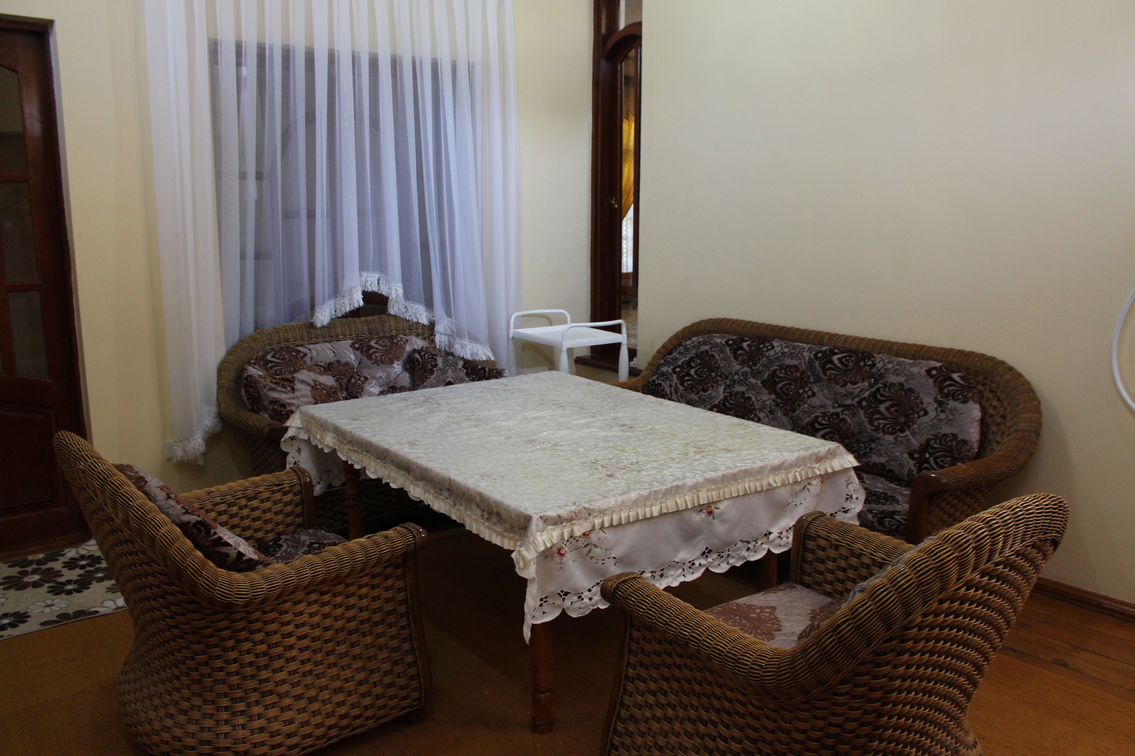 A dining area with a table covered by a lace tablecloth, surrounded by wicker chairs with patterned cushions.