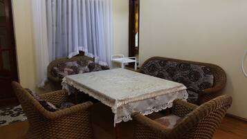 A dining area with a table covered by a lace tablecloth, surrounded by wicker chairs with patterned cushions.