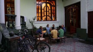 A courtyard with a group of people seated around a table, a bicycle, and a window with a decorative design. - Green House Hostel (Dushanbe)
