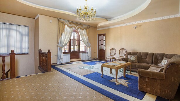 A spacious living room with a large sofa, a coffee table, and a chandelier. There is a window with curtains and a door with glass panels. - Green House Hostel (Dushanbe)