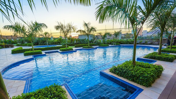A swimming pool with a curved design, surrounded by well-maintained greenery and palm trees. - Mestil Hotels & Residences (Kampala)