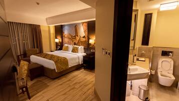 Habitación de hotel con una cama grande, un escritorio, una silla, un baño con inodoro y lavamanos, y un mural en la pared.