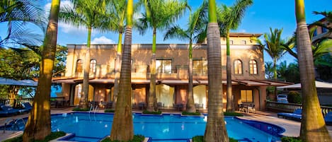 A resort with a swimming pool, palm trees, and a building with multiple windows and balconies.