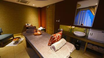 Relax in a serene spa room with a massage table, sink, and comfortable bench.