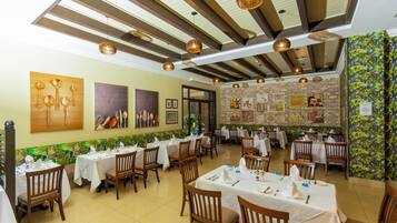 A restaurant with multiple tables and chairs, a high ceiling with wooden beams, and wall art.