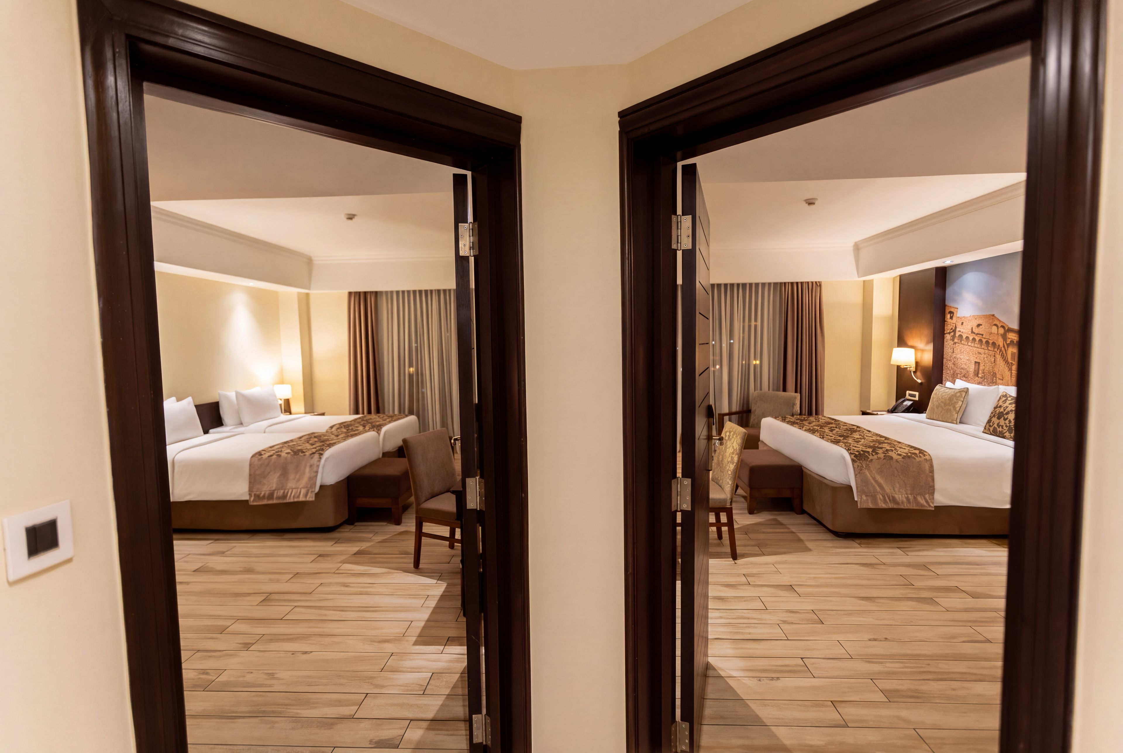 Une chambre d’hôtel dotée d’un grand miroir qui reflète le lit, un bureau et une chaise. La chambre a un plancher en bois et une lampe fixée au mur.