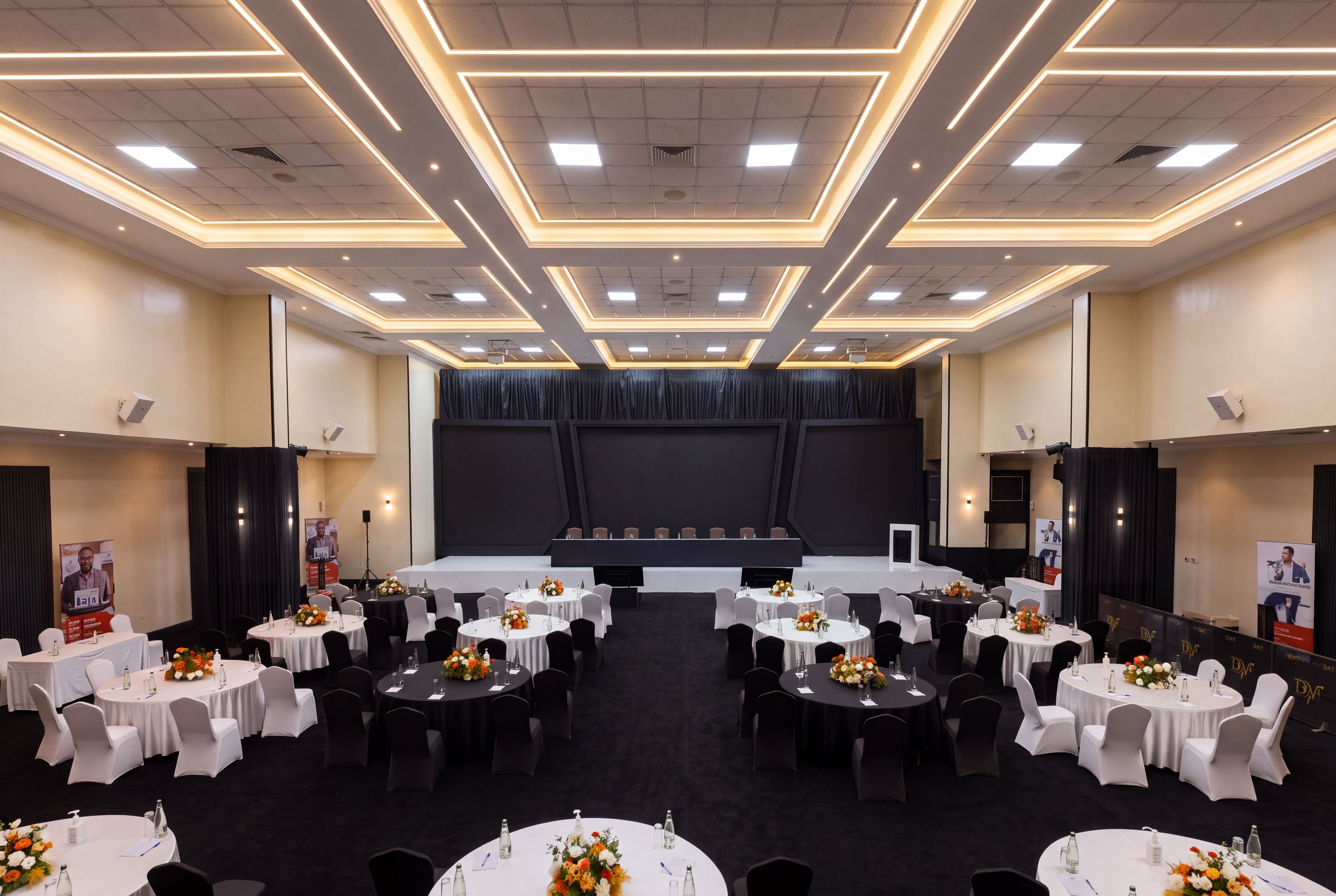 A conference room with multiple round tables, white tablecloths, and black chairs.