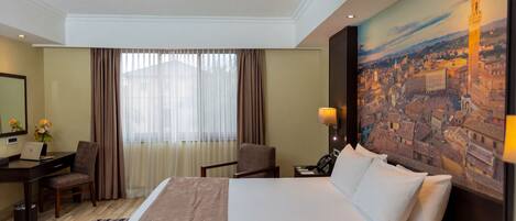 A hotel room with a bed, a desk, a chair, a lamp, and a painting of a cityscape.