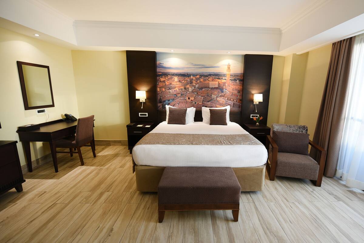 A hotel room with a large bed, a desk, a chair, and a view of a cityscape.