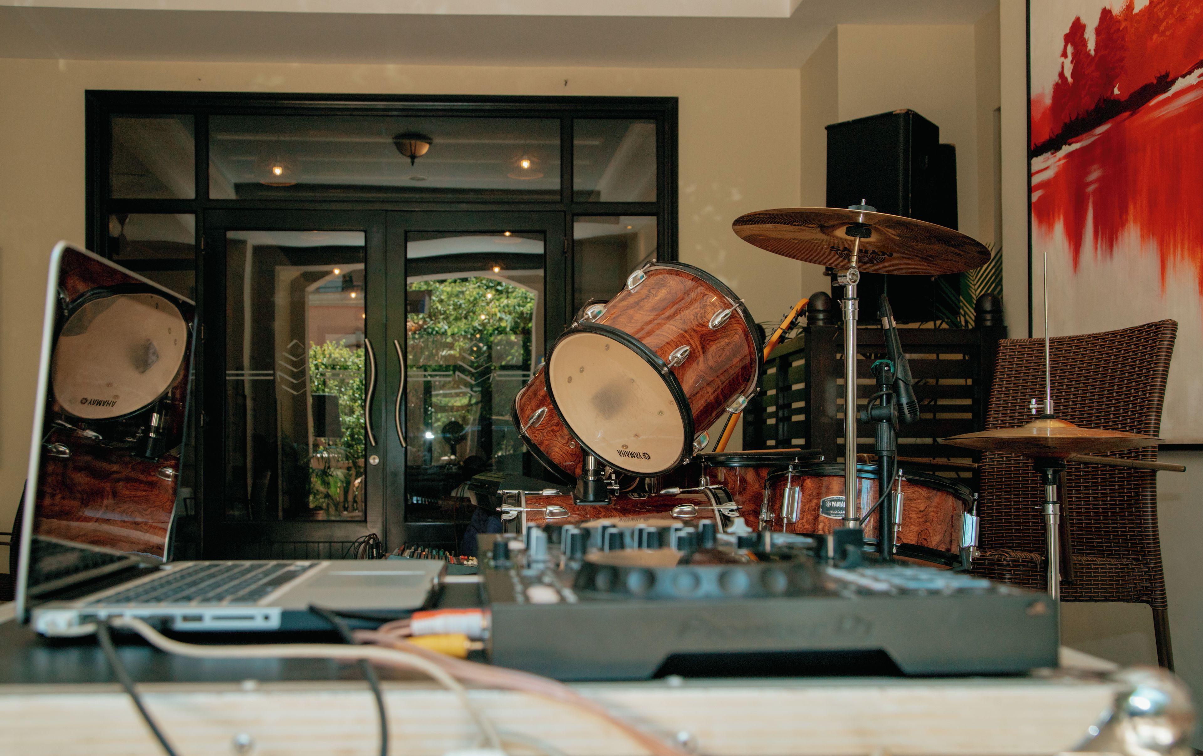 A drum set with a laptop and audio equipment in a room with a large window and a door.