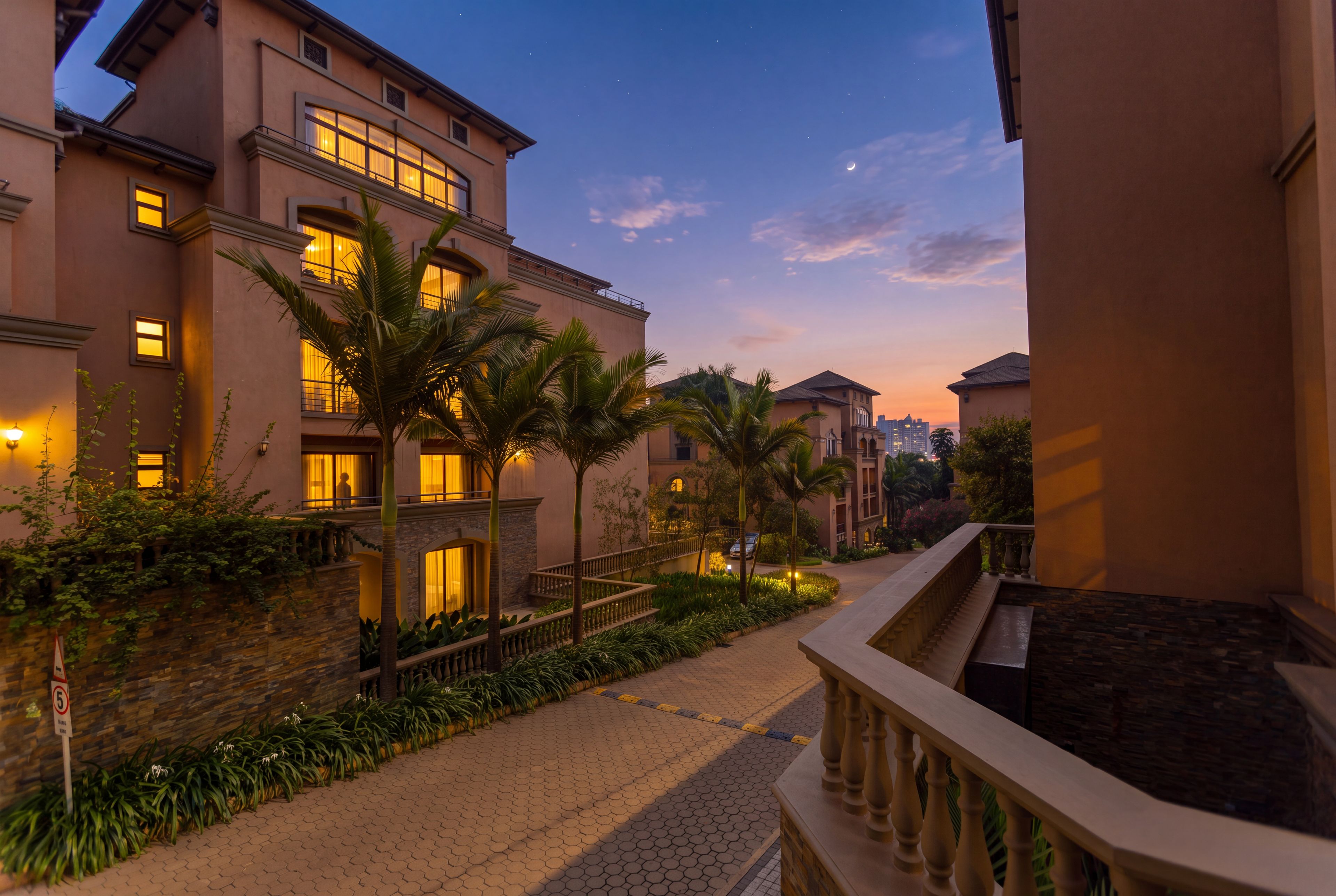 A hotel with multiple floors, a paved walkway, and palm trees.