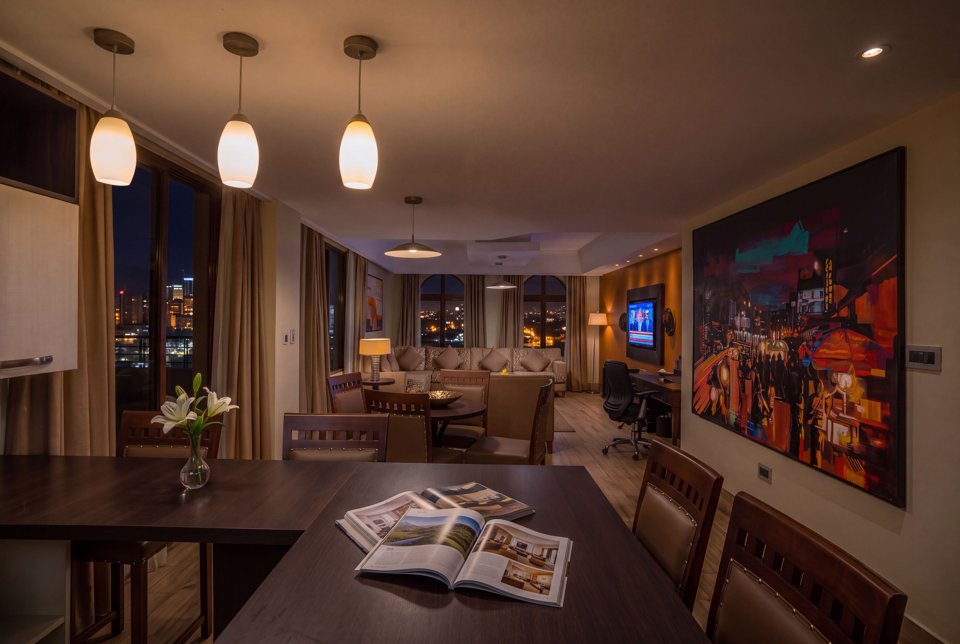 A hotel room with a dining area, a sofa set, a television, and a large painting on the wall.