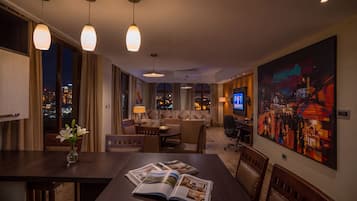 A hotel room with a dining area, a sofa set, a television, and a large painting on the wall.
