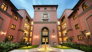 A pink building with a central entrance, multiple windows, and a fountain in the courtyard. - Mestil Hotels & Residences (Kampala)